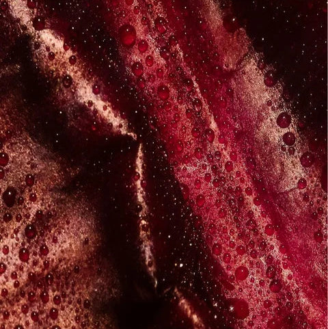 Close-up van vochtige textuur met rode tinten die de rijke samenstelling van Anti-Age Dagcrème symboliseren voor natuurlijke huidverzorging en skincare.