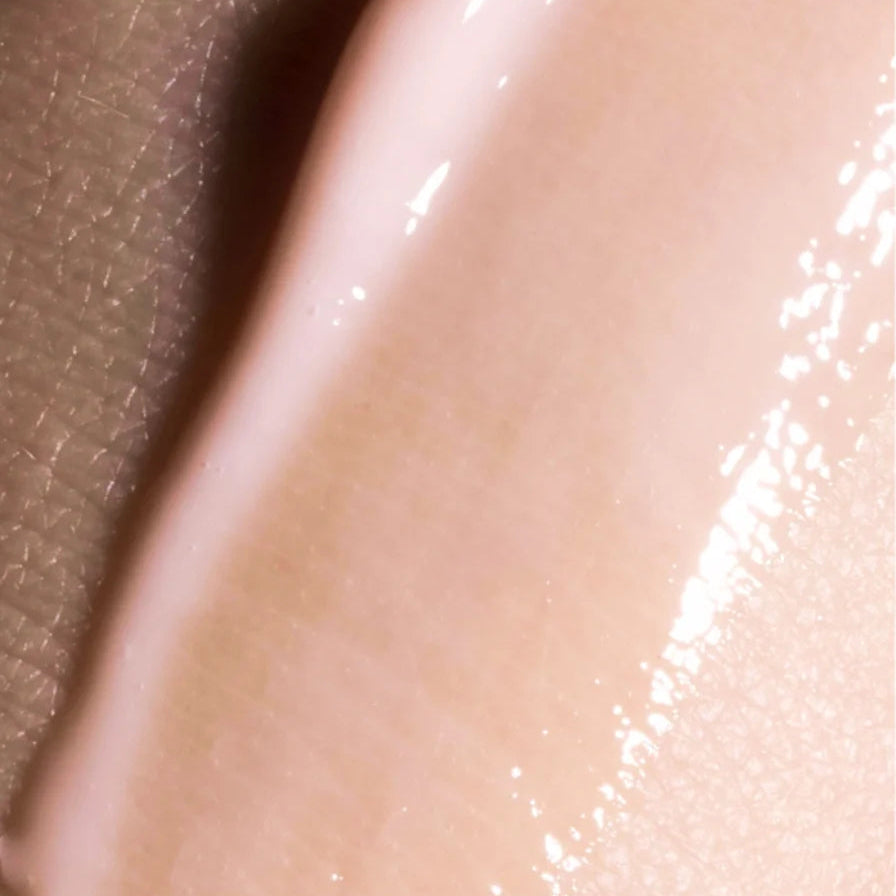 Veloura peptide serum aangebracht op de huid, close-up van glanzende roze geltextuur die hydrateert en de huid een zachte, stralende anti-aging glow geeft.