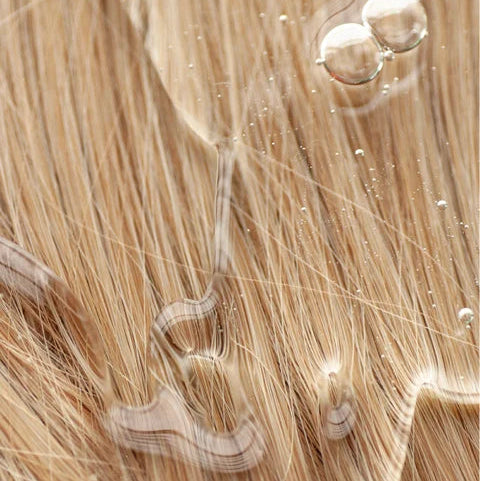 Natuurlijke uitstraling van blond haar met glanzende textuur en waterdruppels, passend bij de verzorgende eigenschappen van Glans Shampoo Smoky Green Vetiver.
